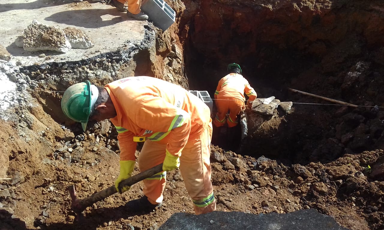 #PraCegoVer - Dois trabalhadores escavam o solo para construção de bocas-de-lobo e caixa de galeria. À esquerda, aparece parte do piso de asfalto que foi desfeito.