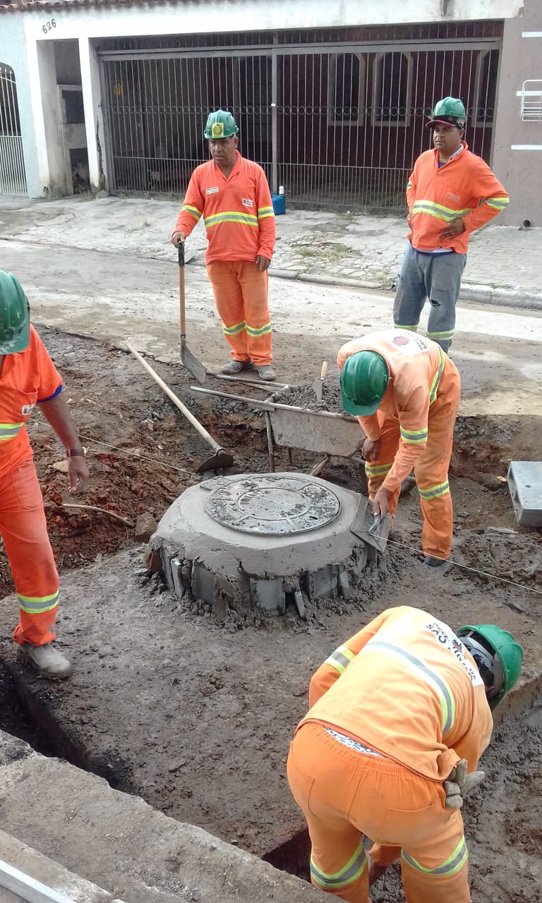 #PraCegoVer - Trabalhadores da Subprefeitura, em macacões cor de laranja finalizam reconstrução de poço   de visita (bueiro) para que fique no nível da rua.