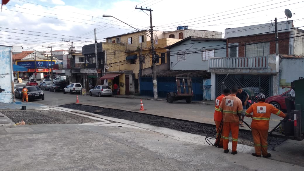 #PraCegoVer - Trabalhadores da Subprefeitura finalizam tapa-buraco na via. É um arremate de reforma de   sarjetão.