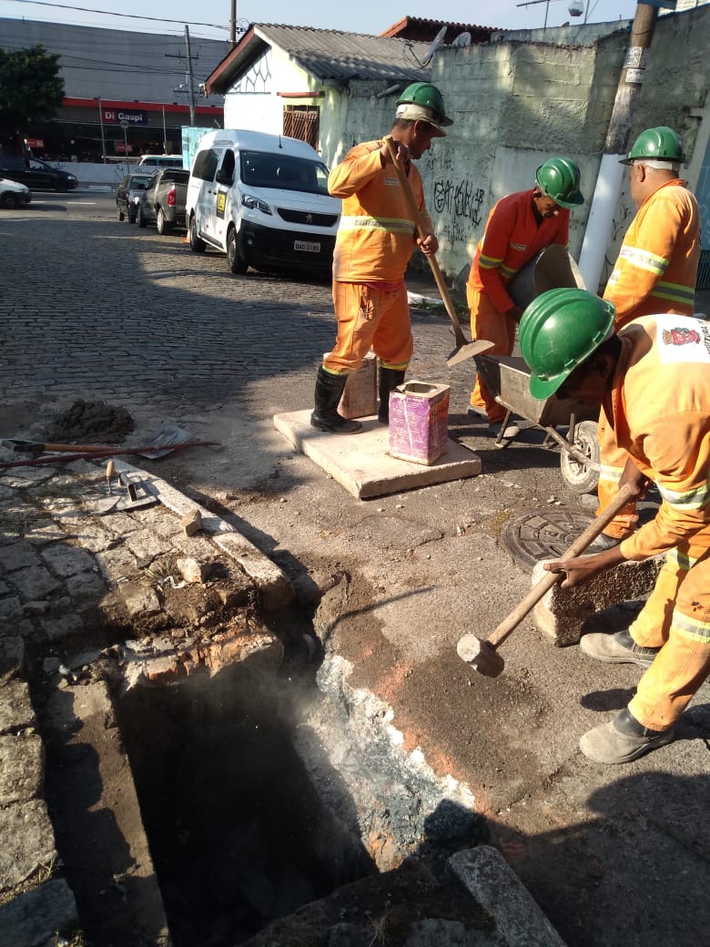 #PraCegoVer - Quatro trabalhadores da Subprefeitura fazem reforma de galerias. O que está em primeiro plano quebra parte da galeria com uma marreta. Os demais preparam massa de cimento para o conserto.