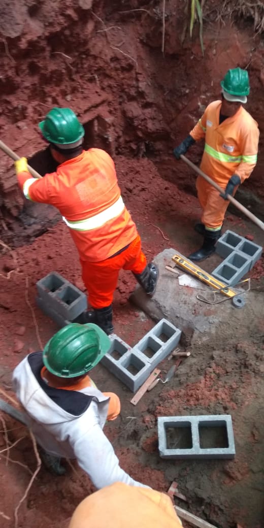 #PraCegoVer - Três trabalhadores da Subprefeitura escavam a via para atingir a Galeria de Águas Pluviais. Há raízes cortadas nas laterais da escavação. E blocos de cimento à espera de colocação