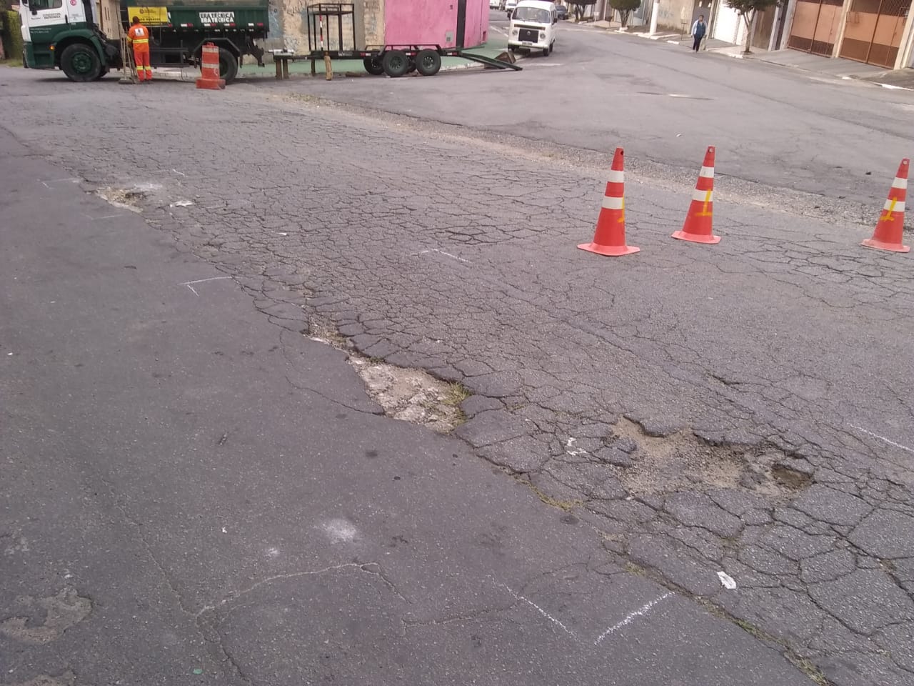 #PraCegoVer - O local fica no entroncamento de duas ruas. O buraco aparece em primeiro plano; na segunda foto, já está tapado. Ao fundo, caminhão da empreiteira que fez o serviço. Mais ao fundo ainda uma Kombi branca.