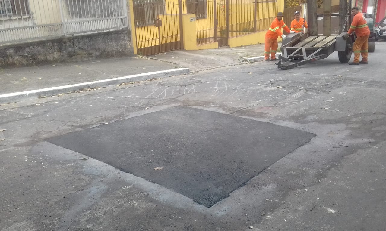 #PraCegoVer - Na primeira foto, trabalhador da Subprefeitura maneja máquina de corte de asfalto, para preparar o piso. Ao fundo, há uma casa toda amarela (paredes e muro). Na segunda foto, o buraco já tapado.