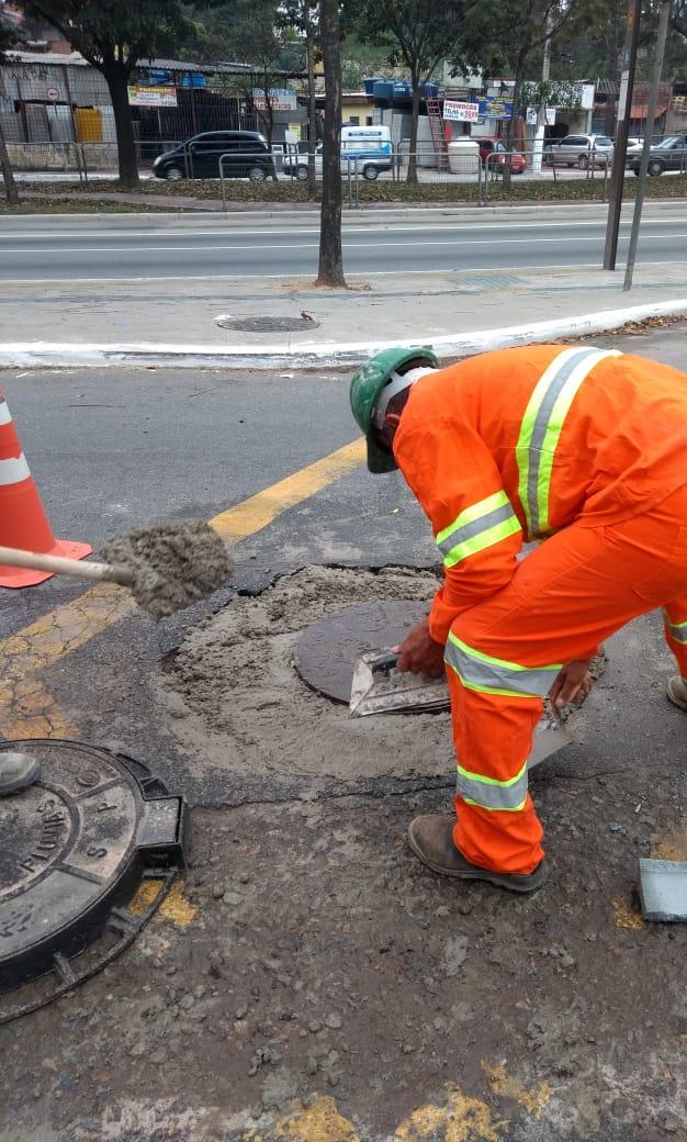 #PraCegoVer - Trabalhador da Subprefeitura faz retoques no piso em torno do poço-de-visita (PV), que foi levantado. Há um cone laranja e branco do lado esquerdo. Ao fundo, a avenida Teotônio Vilela, da qual a rua Pedro de Andrade Caminha é uma espécie de marginal.