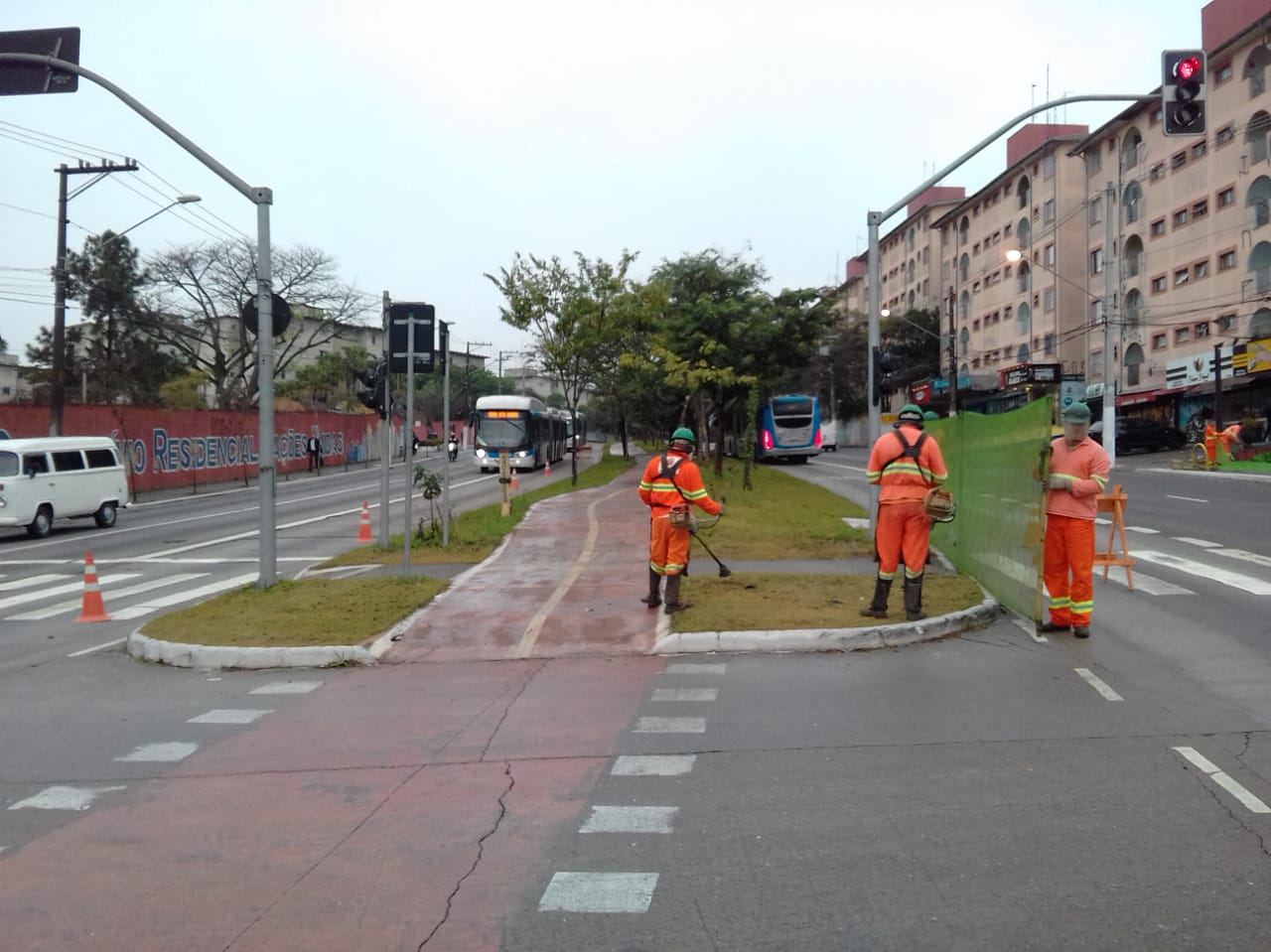 #PraCegoVer - Trabalhadores da Subprefeitura na avenida Teotônio Vilella, Grajaú. Dois cortam a grama do canteiro central com roçadeiras portáteis; outros dois sustentam a tela de proteção. No local, há um semáforo. Ao fundo há um prédio de apartamentos, à direita.