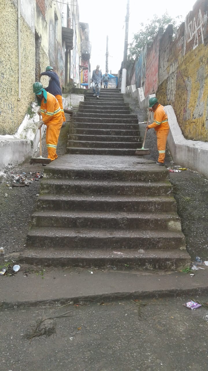 #PraCegoVer - Trabalhadores da Subprefeitura limpam o escadão, como preparação para os trabalhos de recuperação da obra. O escadão foi fotografado de baixo para cima. Há dois paredões, um de cada lado.