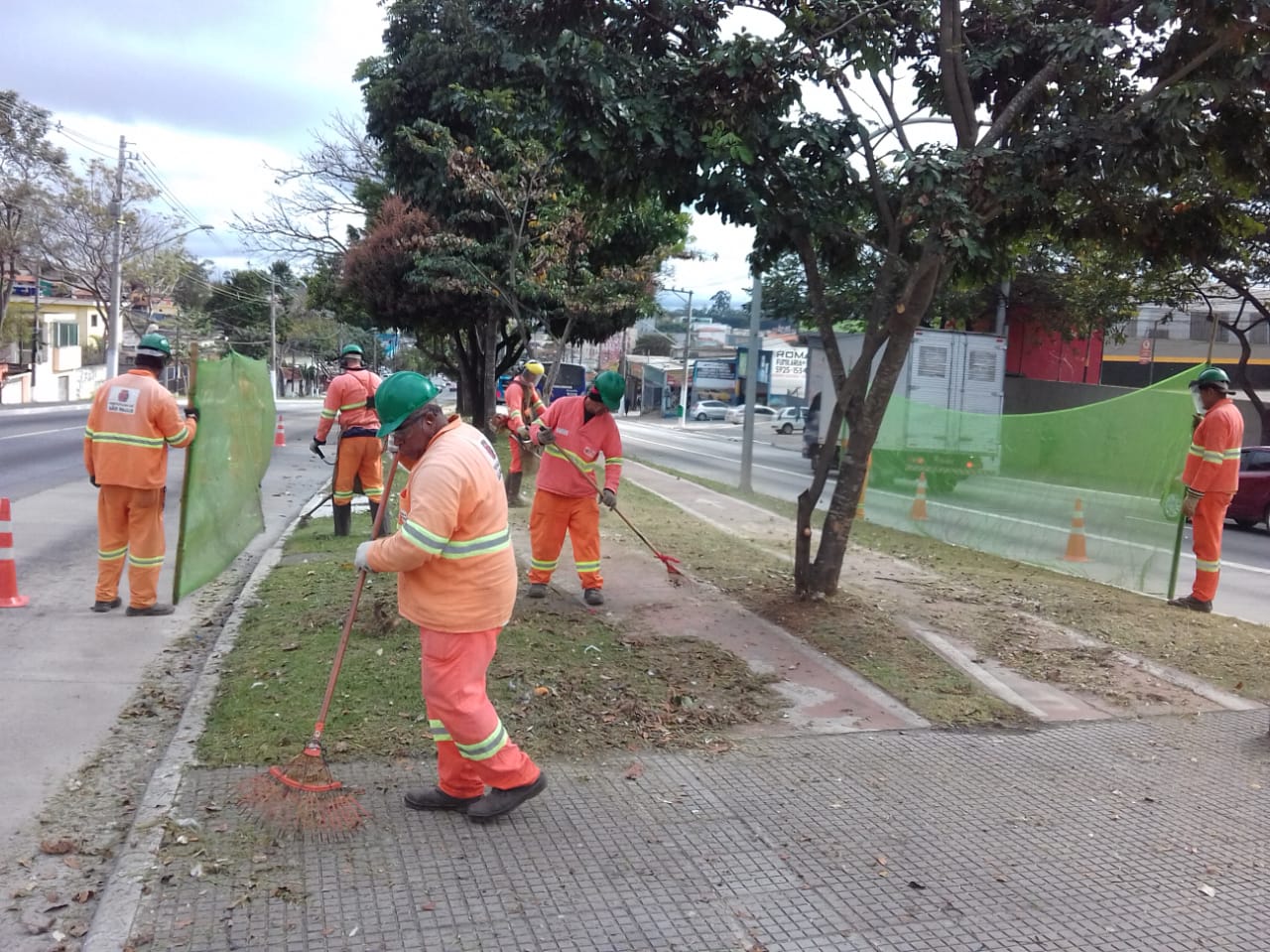 #PraCegoVer - Trabalhadores da Subprefeitura cortam grama no canteiro central da avenida Teotônio Vilella. Quatro homens seguram proteção de tela. Dois fazem o corte. Outros dois rastelam a grama cortada.