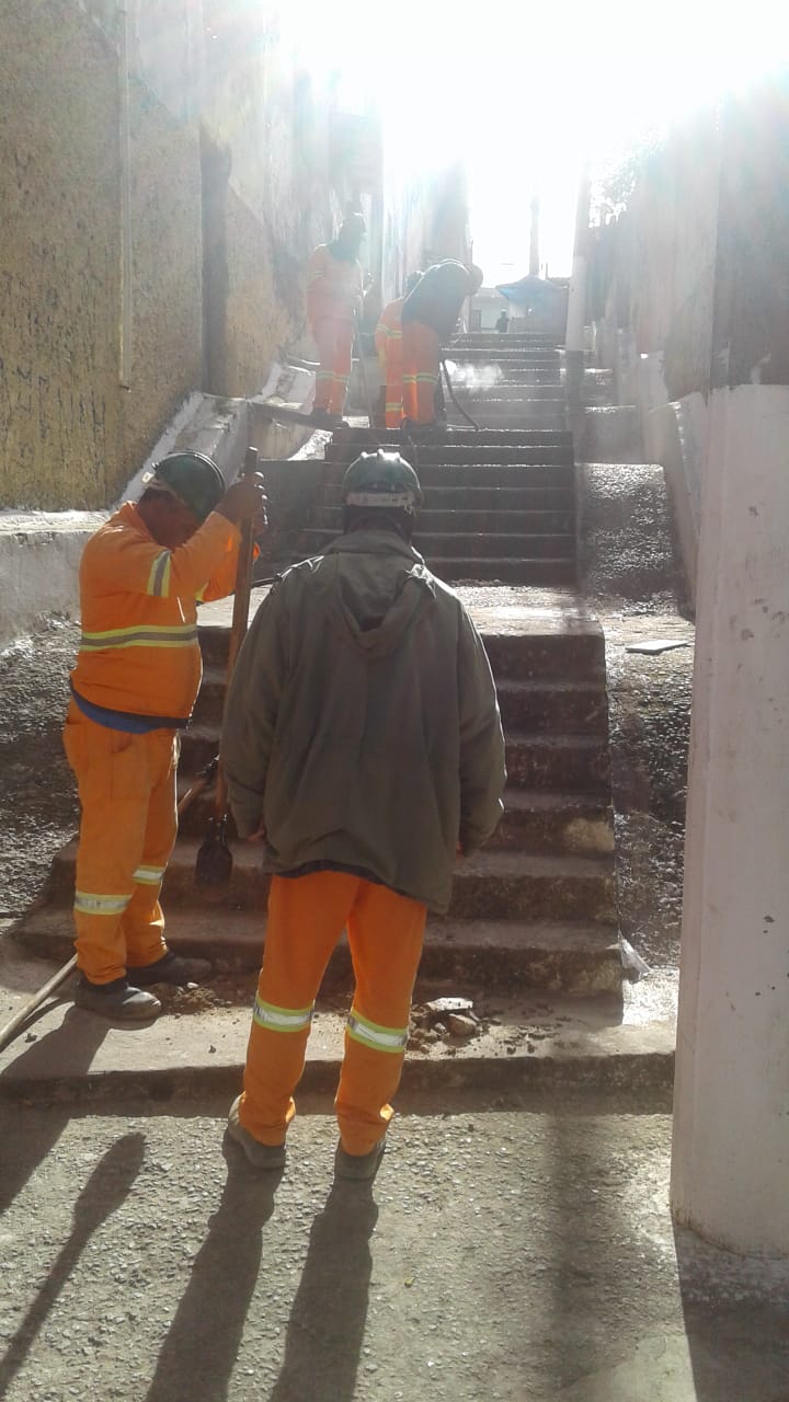#PraCegoVer - Cinco trabalhadores da Subprefeitura verificam a estrutura do escadão. Há paredes dos dois lados.