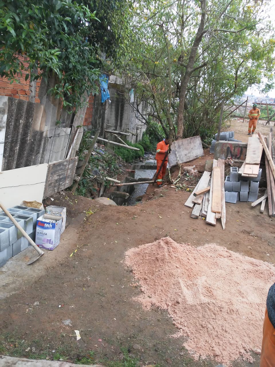 #PraCegoVer - Trabalhadores da Subprefeitura preparam o local, em torno do córrego, para os serviços na galeria. À direita, há um pequeno monte de areia. 