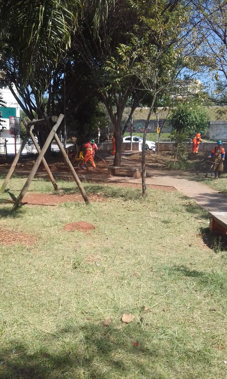 #PraCegoVer - Trabalhadores da Subprefeitura cortam a grama da praça e limpam os restos de grama. Há um balanço do lado esquerdo. Ao fundo, árvores e casas.