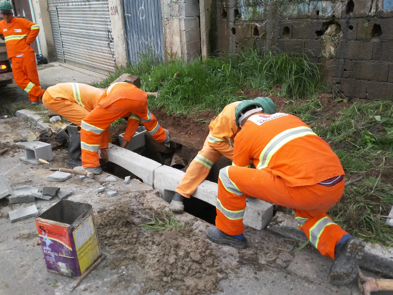 #PraCegoVer - Trabalhadores da Subprefeitura instalam guias-chapéu na boca-de-lobo. A guia-chapéu tem uma curvatura sobre a galeria.