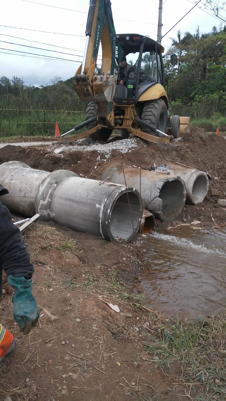 #PraCegoVer - Escavadeira verde e amarela recobre de terra os tubos de concreto na travessia de carros e pedestres.