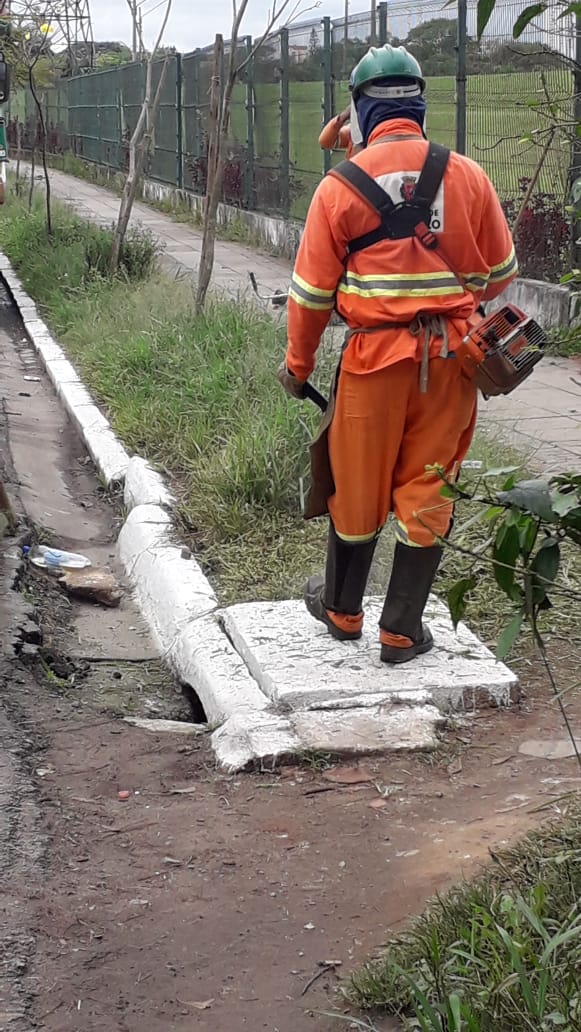 #PraCegoVer - Trabalhador da Subprefeitura corta grama no passeio da via, com uma roçadeira portátil.