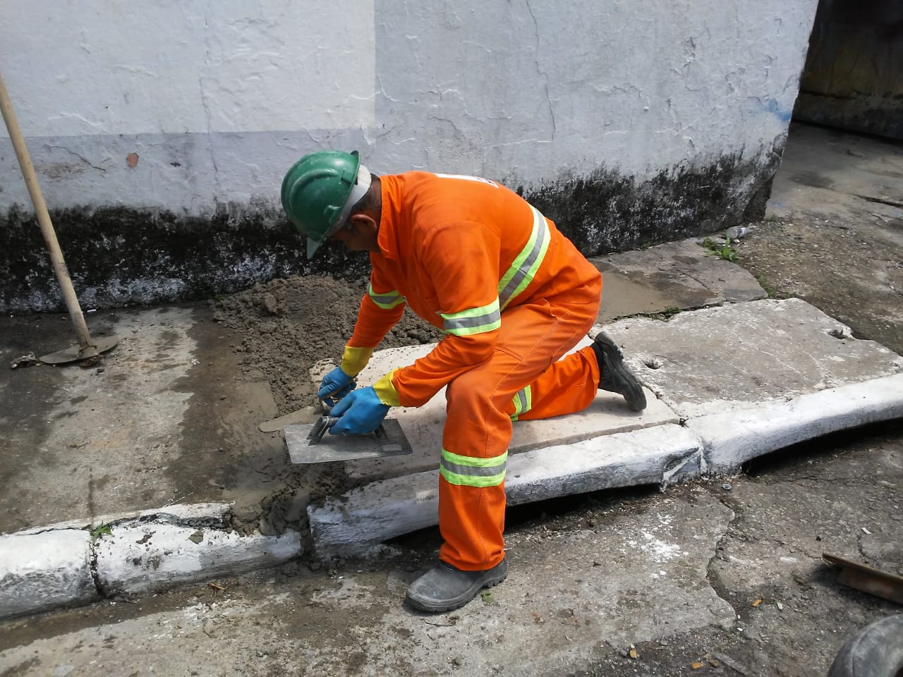 #PraCegoVer - Trabalhador da Subprefeitura arremata com cimento as tampas da boca-de-lobo.