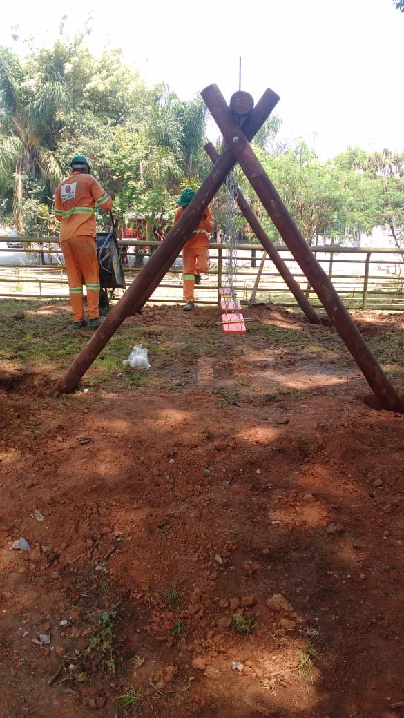 #PraCegoVer - Trabalhadores da Subprefeitura instalam os bancos dos balanços do parque. O suporte são madeiras de tronco trançadas.