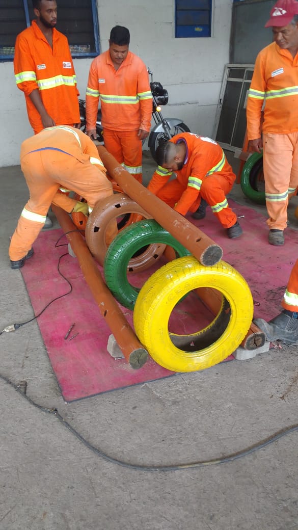 #PraCegoVer - Trabalhadores da Subprefeitura montam um brinquedo composto por três canos; no centro, pneus velhos pintados de várias cores -- amarelo, verde, marron.