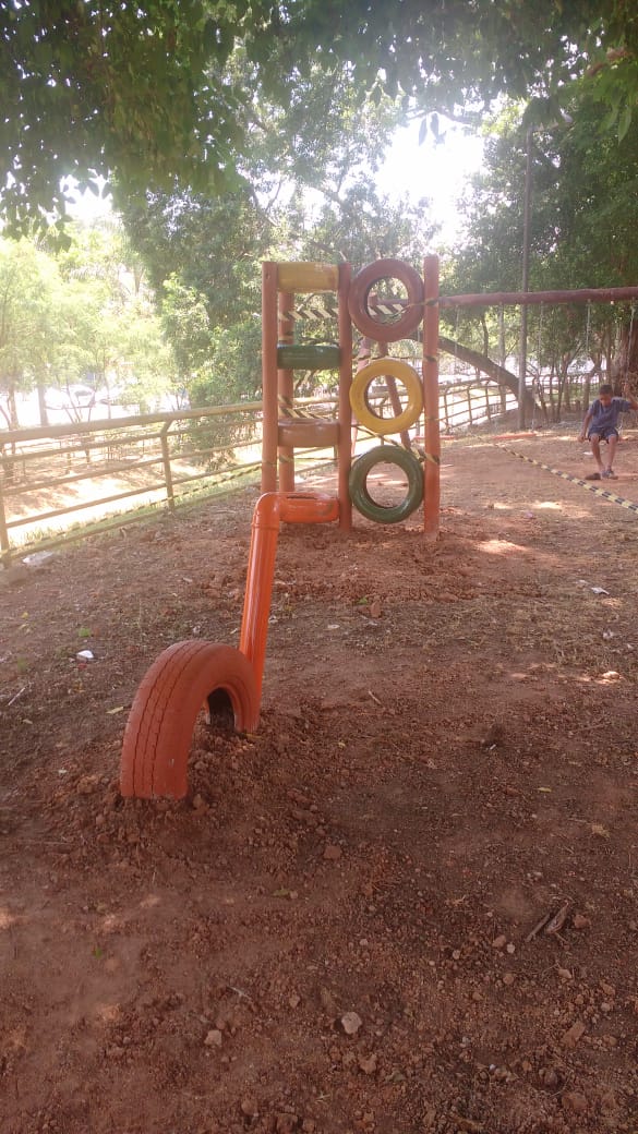 #PraCegoVer - Brinquedos instalados no pequeno parque no local. Um dos brinquedos empilha na horizontal pneus pintados de cores fortes. Um outro brinquedo, ao lado, empilha os pneus na vertical.