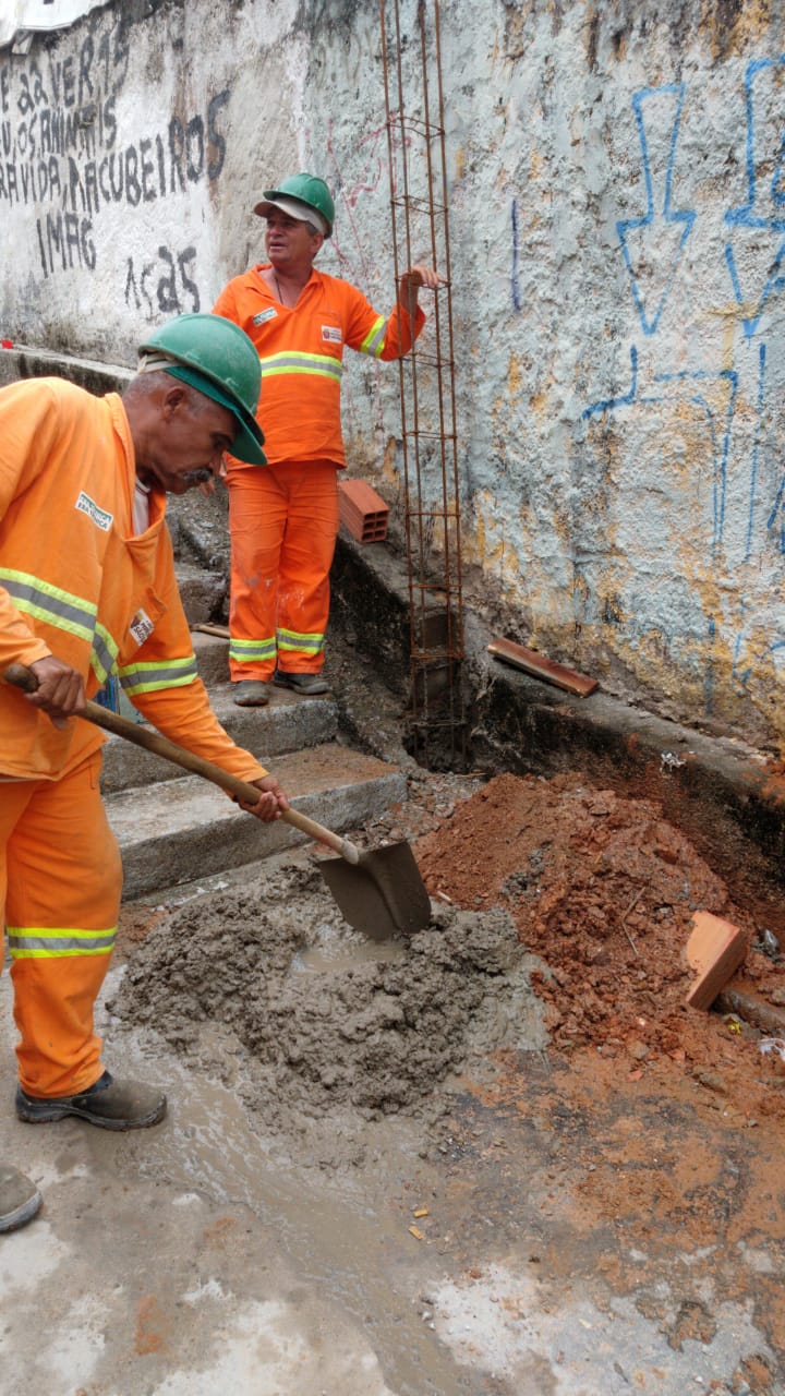 #PraCegoVer - Trabalhadores da Subprefeitura misturam cimento. Outro sustenta armação de ferro para coluna.