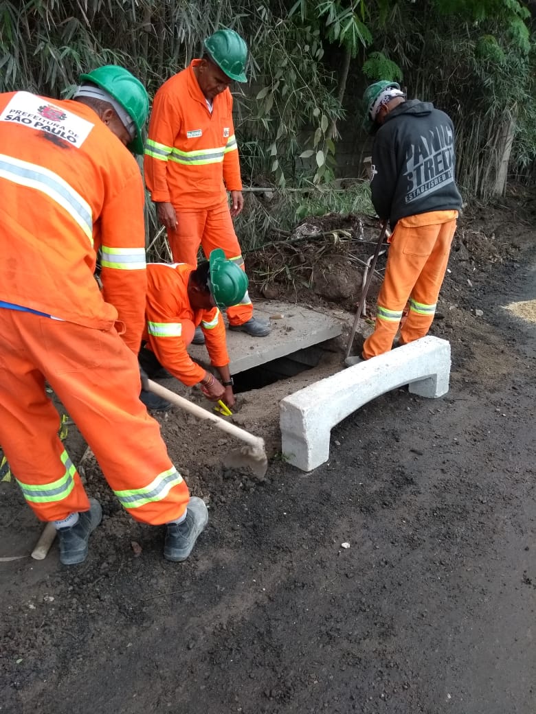 #PraCegoVer - Trabalhadores da Subprefeitura preparam o local em que será colocada uma nova guia-chapéu. A guia nova está de lado: trata-se de uma guia com espaço para escoamento de água.