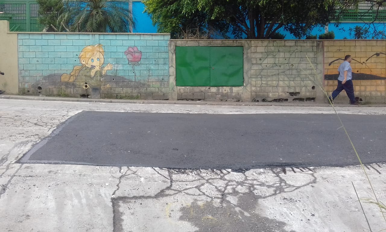 #PraCegoVer - Na primeira foto, o buraco em preparação. A via está diante de um muro com um grafitti com um menino e uma flor. Na segunda foto, o buraco já tapado.