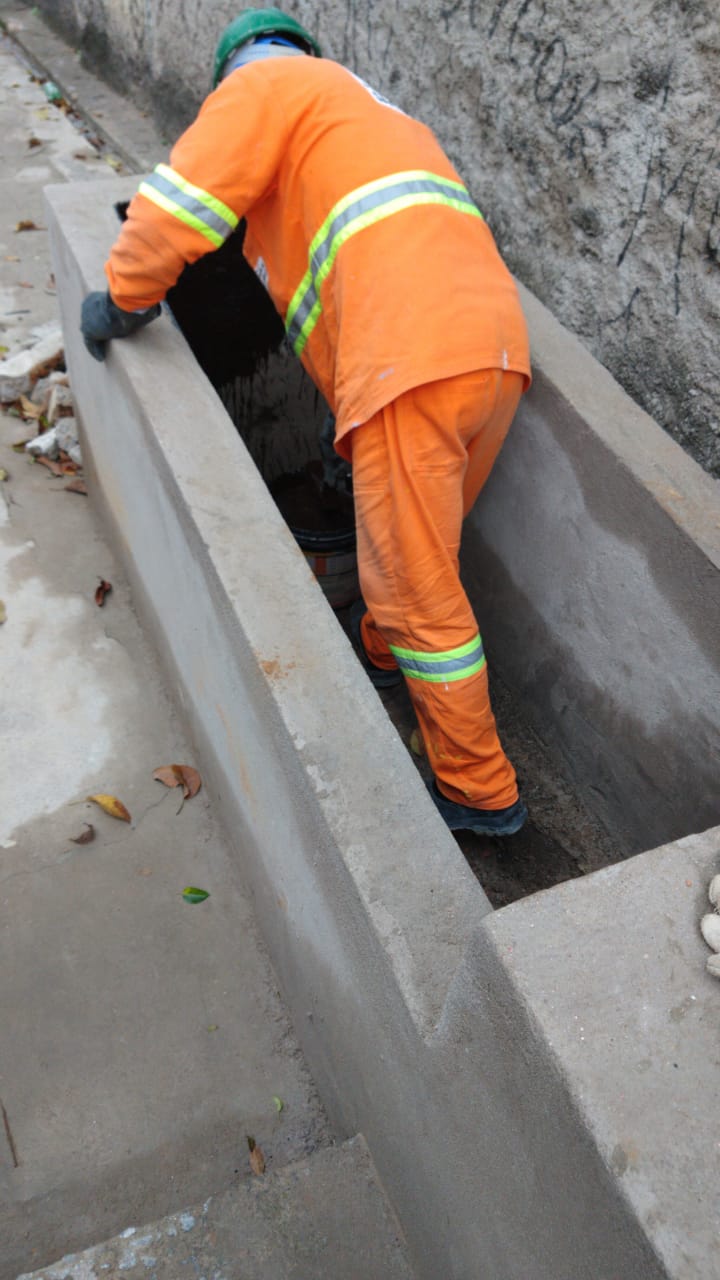 #PraCegoVer - Trabalhador da Subprefeitura aplica produto impermeabilizante no depósito de água de chuva na viela.