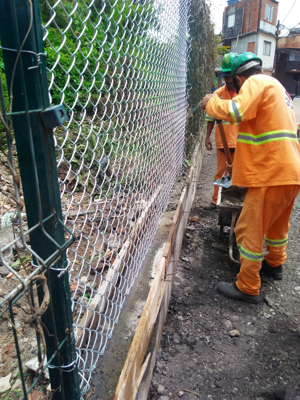 #PraCegoVer - Trabalhadores da Subprefeitura instalam tela de arame, para consertar parte da cerca, derrubada. A base é feita de alvenaria.