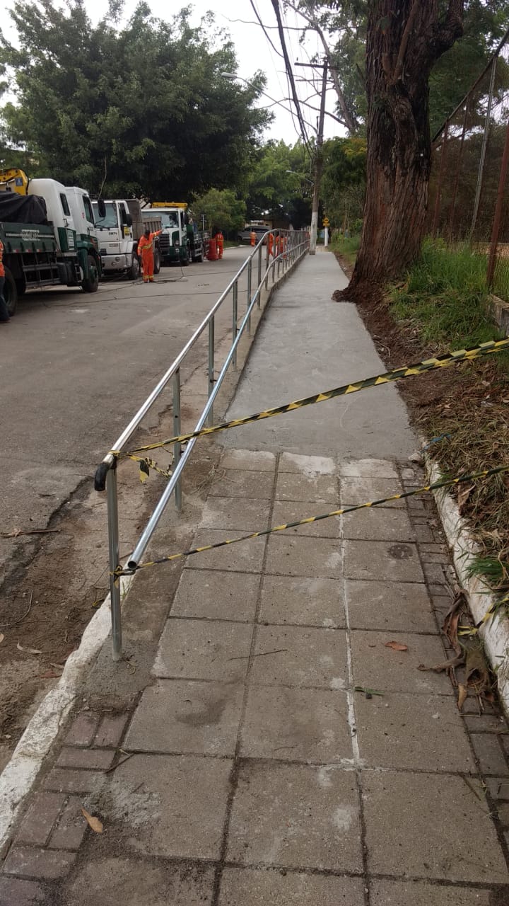 #PraCegoVer - Calçada reformada, com novo corrimão instalado. O acesso está restrito por faixas de riscas amarelas e pretas enquanto o concreto seca.