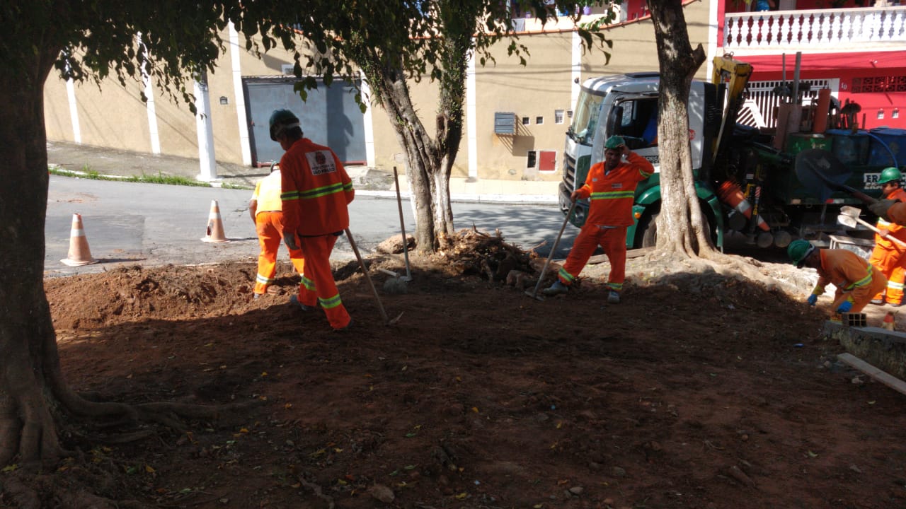 #PraCegoVer - Trabalhadores da Subprefeitura limpam o local. Há árvores e casas ao fundo.