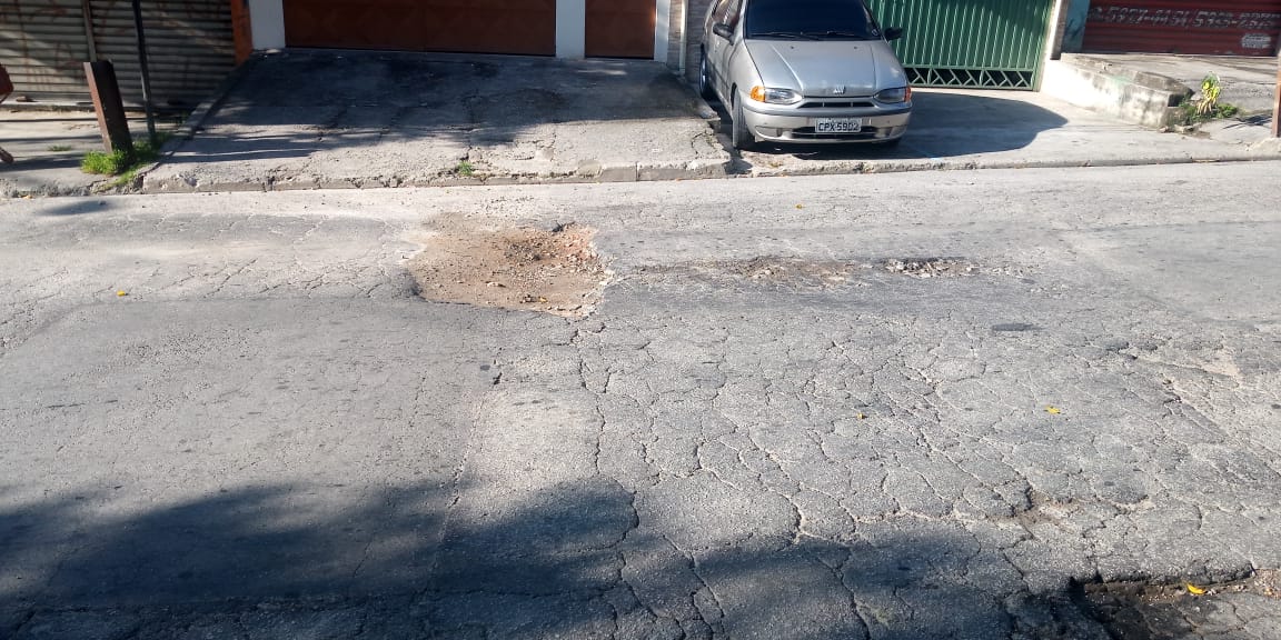 #PraCegoVer - Na primeira foto, o buraco na via. Ao fundo, casas e um carro estacionado. Na segunda foto, o buraco já tapado.