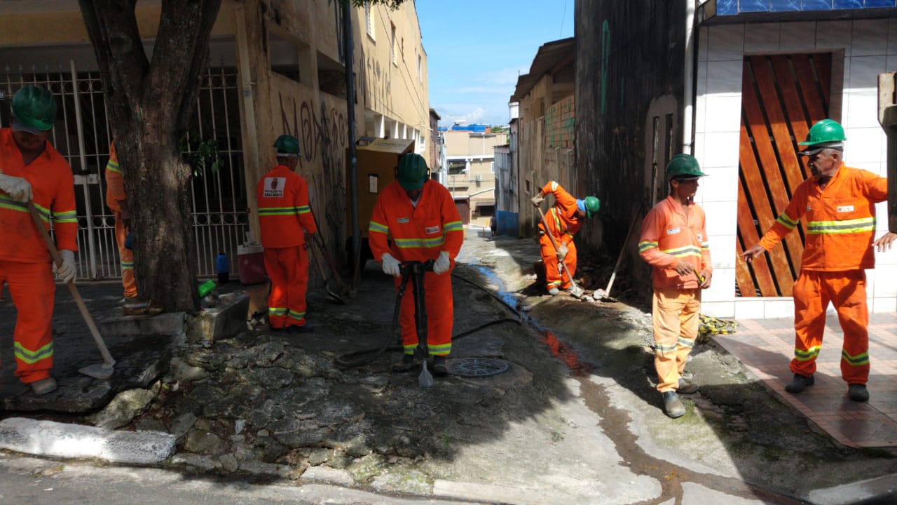 #PraCegoVer - Trabalhadores da Subprefeitura reformam a viela entre duas fileiras de casas.