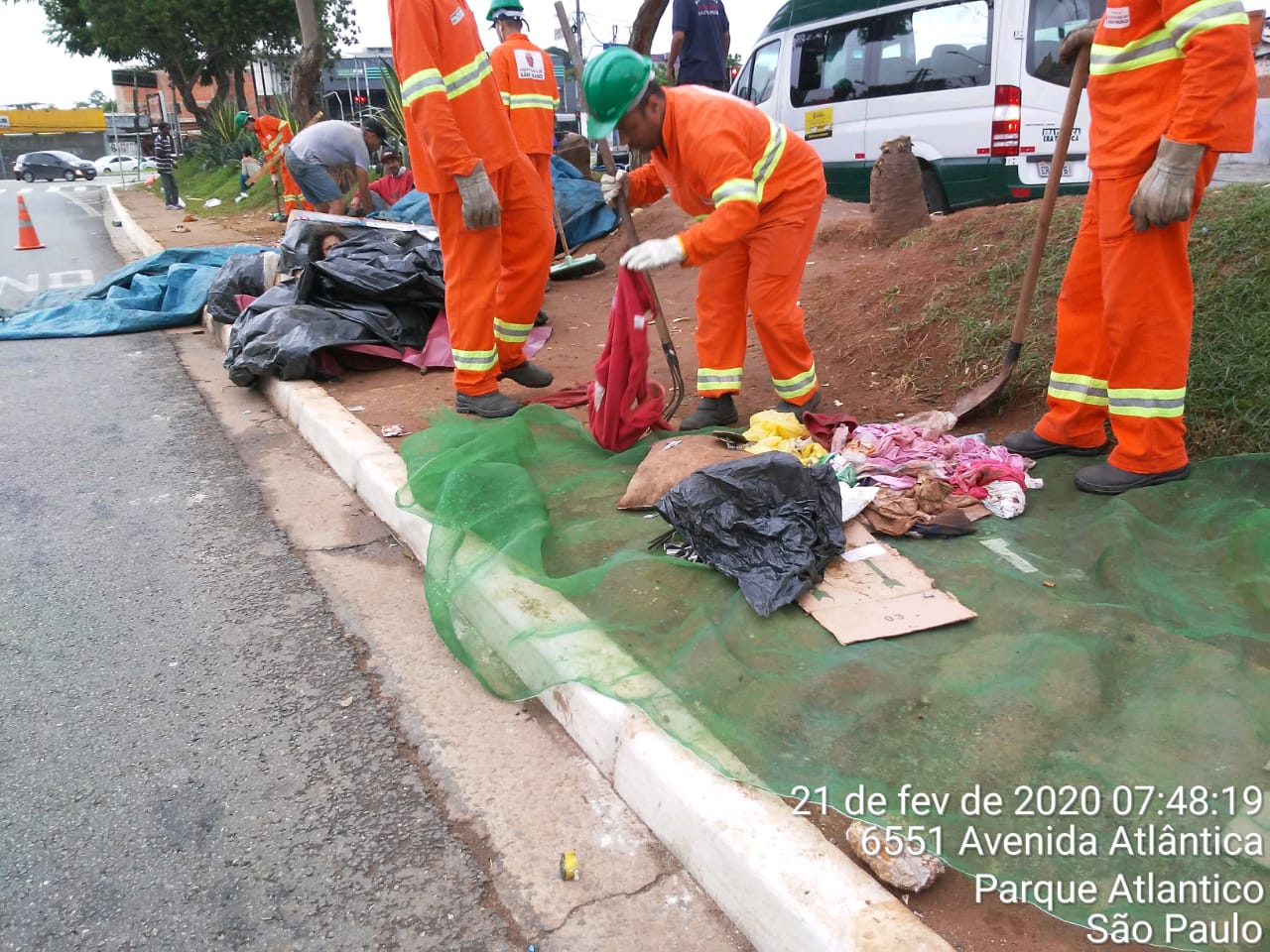 #PraCegoVer - Trabalhadores da Subprefeitura recolhem material no canteiro central da via.