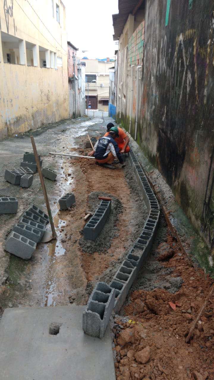 #PraCegoVer - Trabalhadores da Subprefeitura assentam blocos de concreto como base do passeio de viela.
