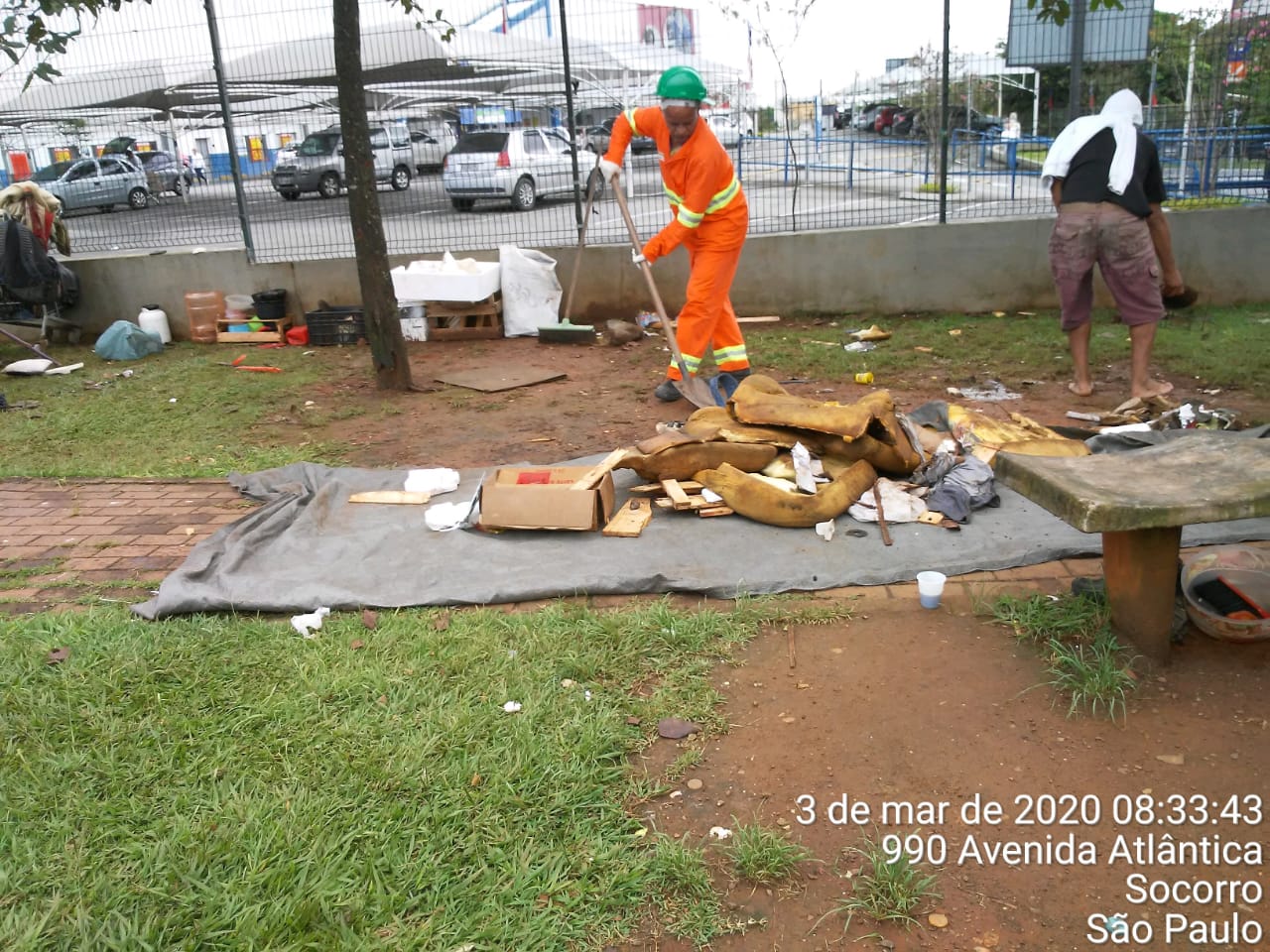 #PraCegoVer - Trabalhador da Subprefeitura varre e recolhe material deixado por moradores de rua. Há um alambrado ao fundo.