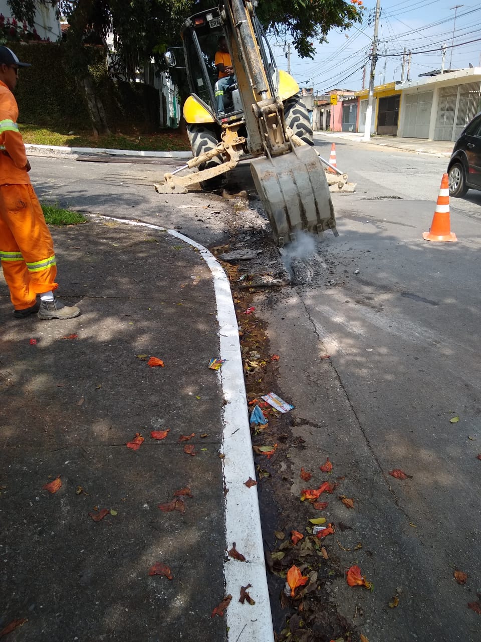 #PraCegoVer - Escavadeira abre o piso na esquina de duas ruas. O local está sinalizado por cones.