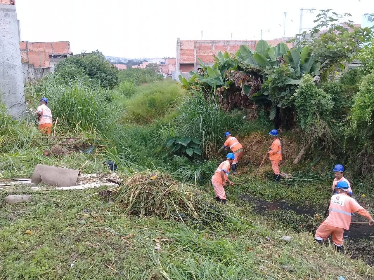 #PraCegoVer - Trabalhadores da Subprefeitura limpam a vegetação dos dois lados do córrego