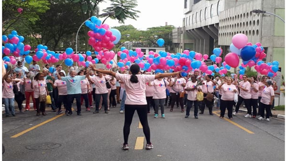 Multidão de pessoas de braços abertos segurando balões da cor rosa e azul.