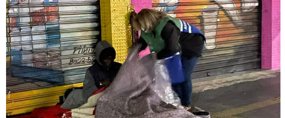 Uma mulher da Assistência Social ajuda e distribui coberto para morador de rua.