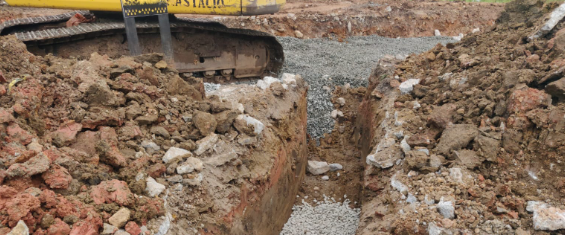 Valeta cavada por escavadeira está coberto por brita ao fundo. Nos dois lados, terra misturada com entulho está amontoada.