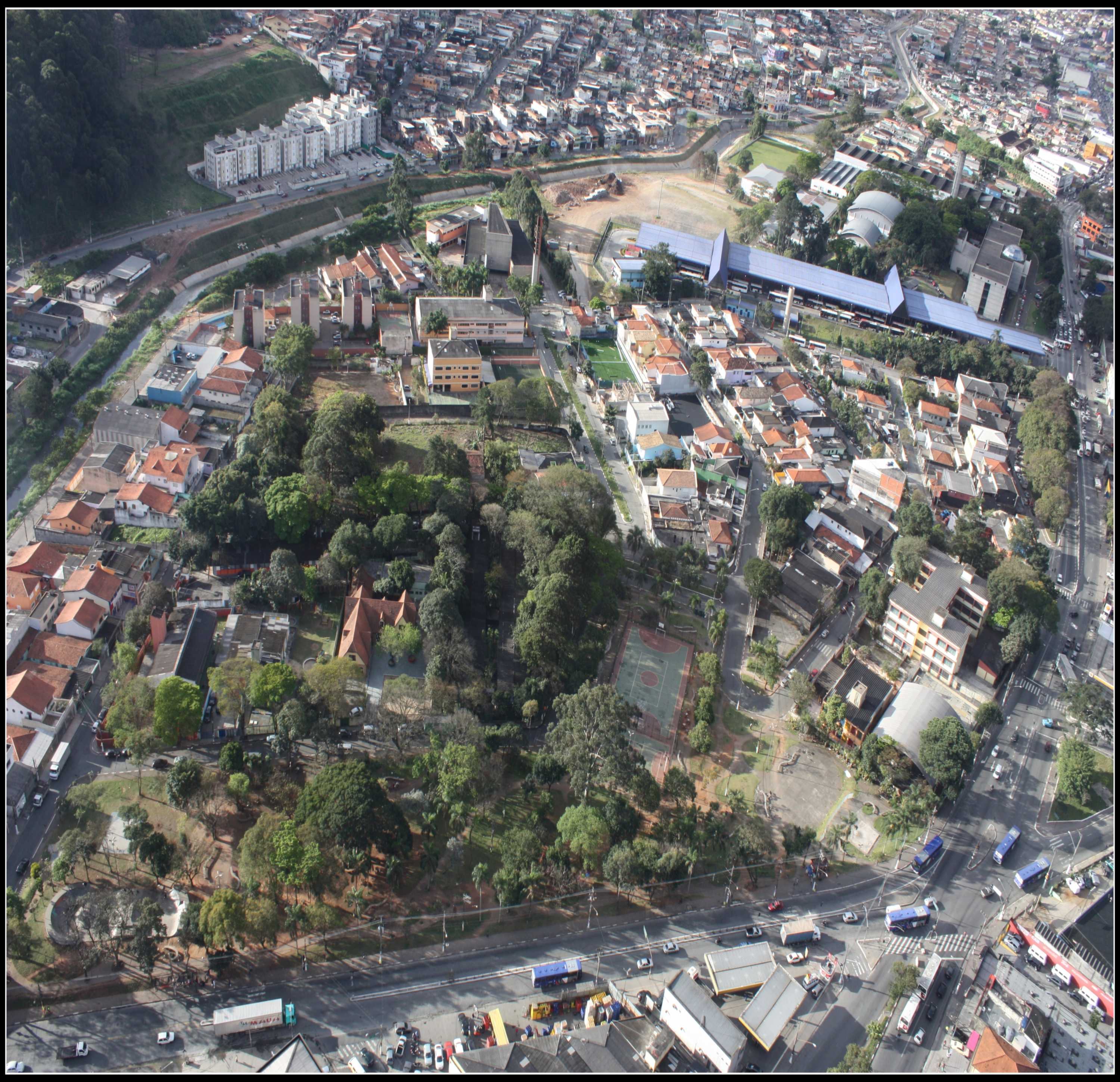 A imagem apresenta uma foto aérea da região do distrito de Campo Limpo. Ela possui carros, árvores, uma praça, diversas casas, prédios e caminhos de ruas.