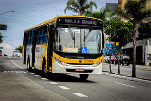 #PraCegoVer : A foto apresenta o ônibus amarelo da Prefeitura de São Paulo em movimento na Av. São Miguel