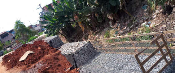 Um muro de pedras colocadas em uma gaiola de arame foi construído em um trecho de margem do córrego. Do outro lado, uma fileira de bananeiras.