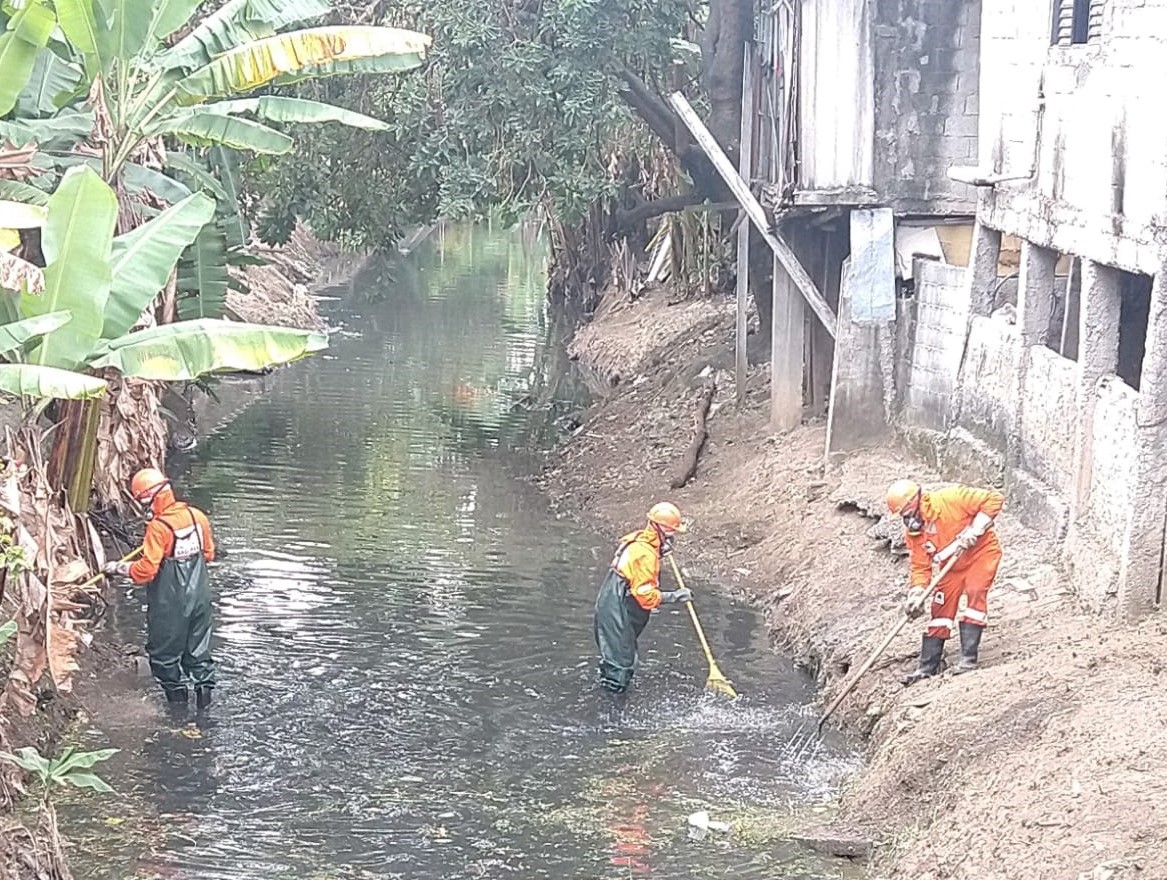 Trabalhadores com equipamentos de segurança e usando macacões de saneamento que protegem contra contaminação fazendo limpeza de córrego