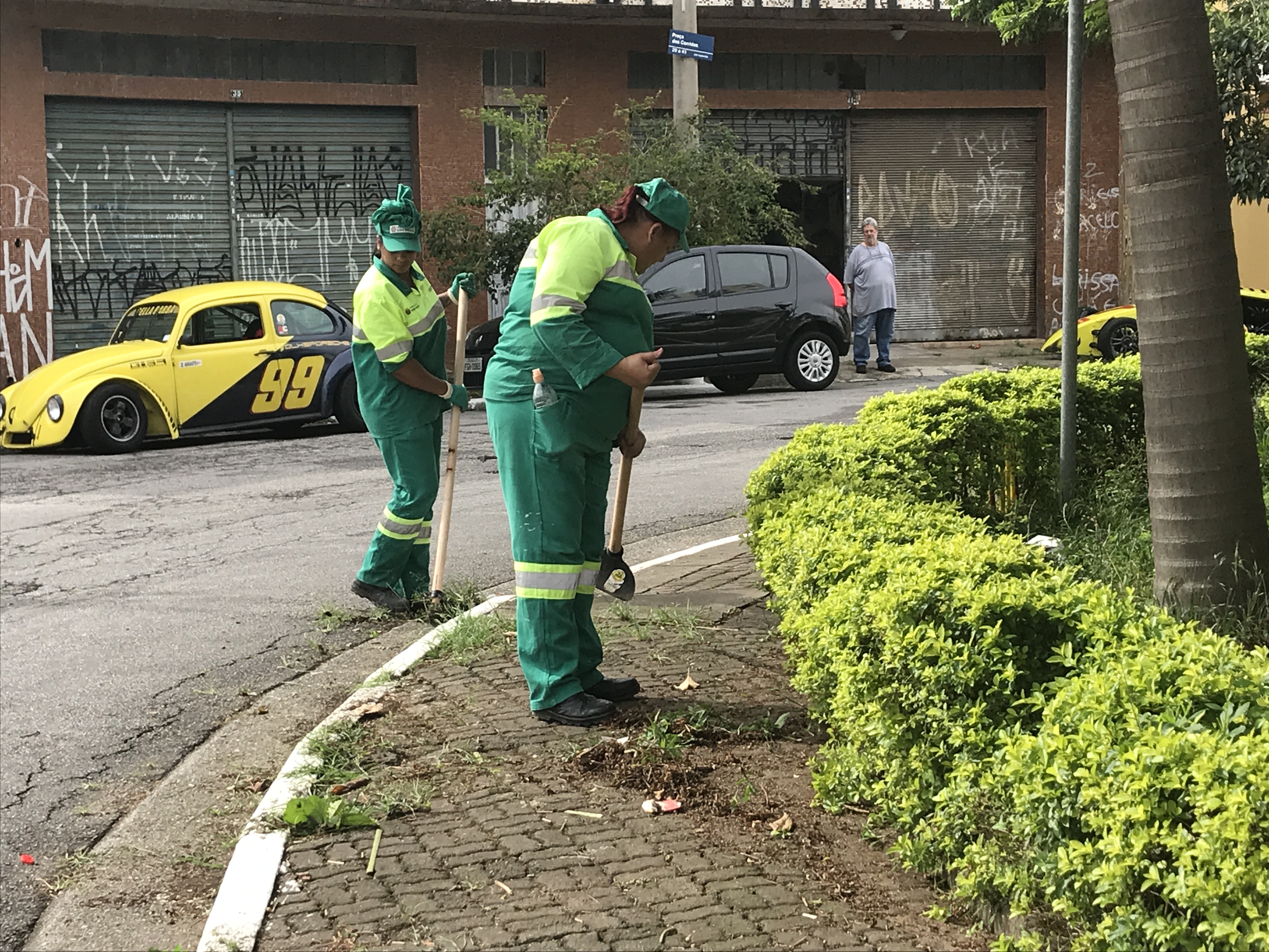 Duas trabalhadoras limpando a  calçada da praça