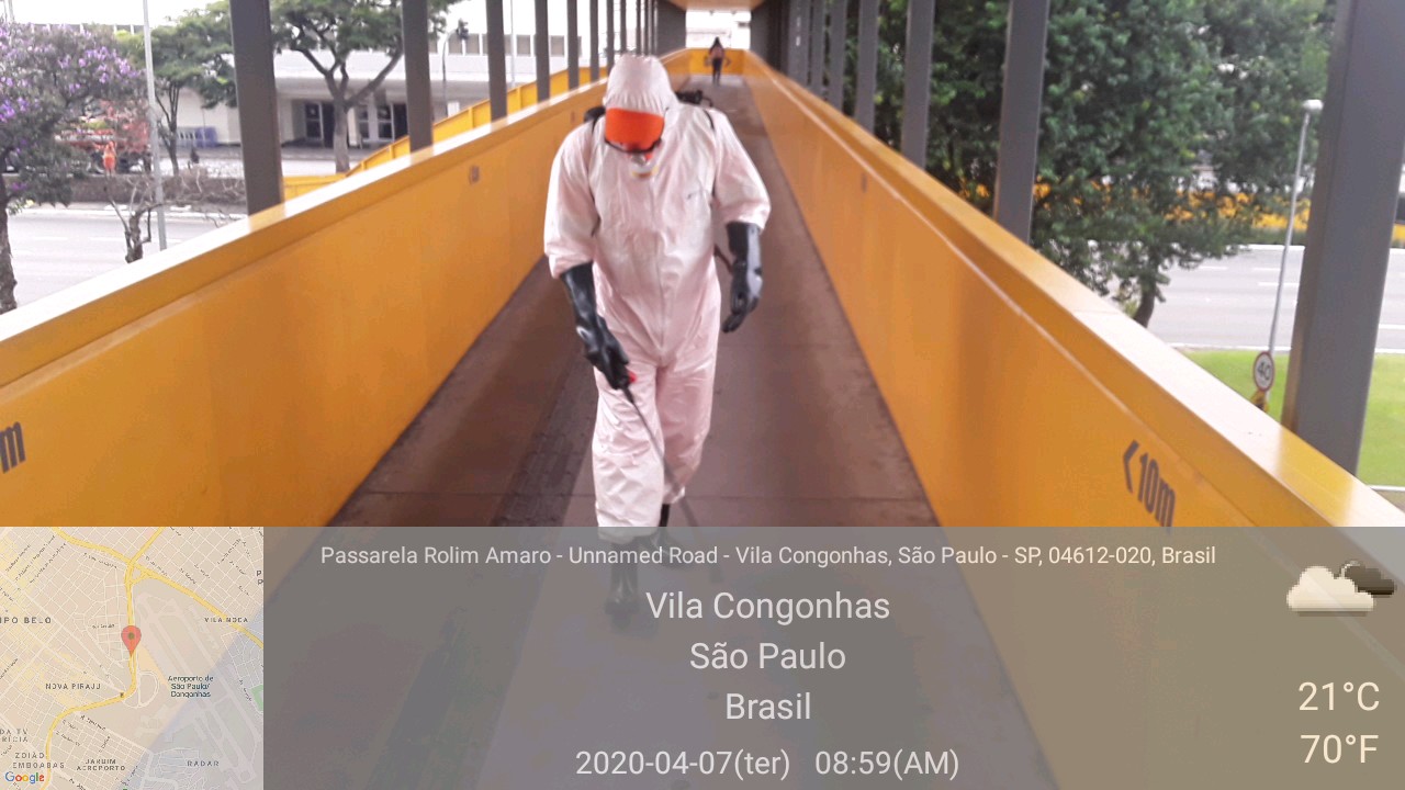 Imagem de um funcionário da prefeitura usando máscara e macacão de proteção e com uma máquina de jato d`água, realizando a limpeza e higienização, de uma passarela de pedestres.