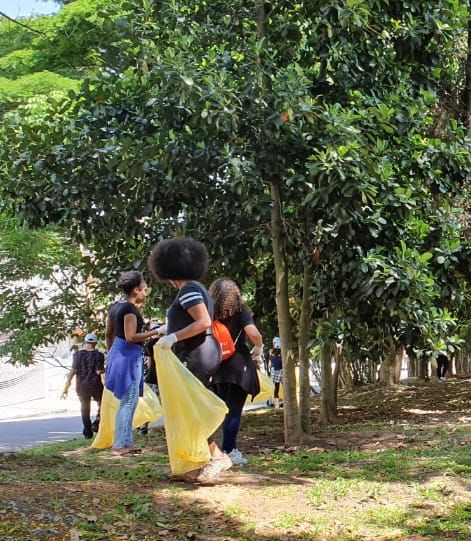 Garotas coletam lixo lançado sobas árvores