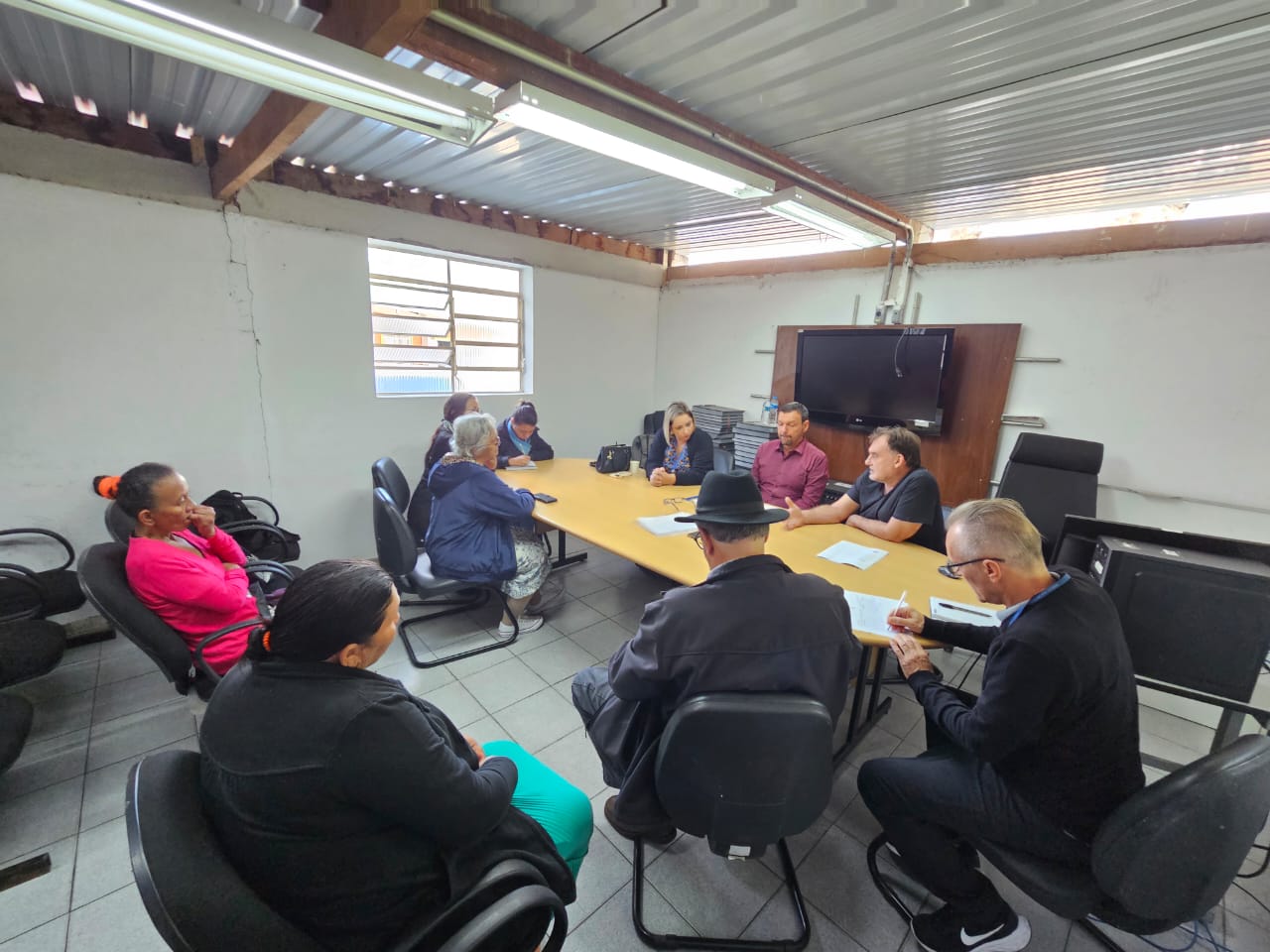 Grupo de pessoas reunidas em torno de uma mesa e sentadas em cadeiras próximas