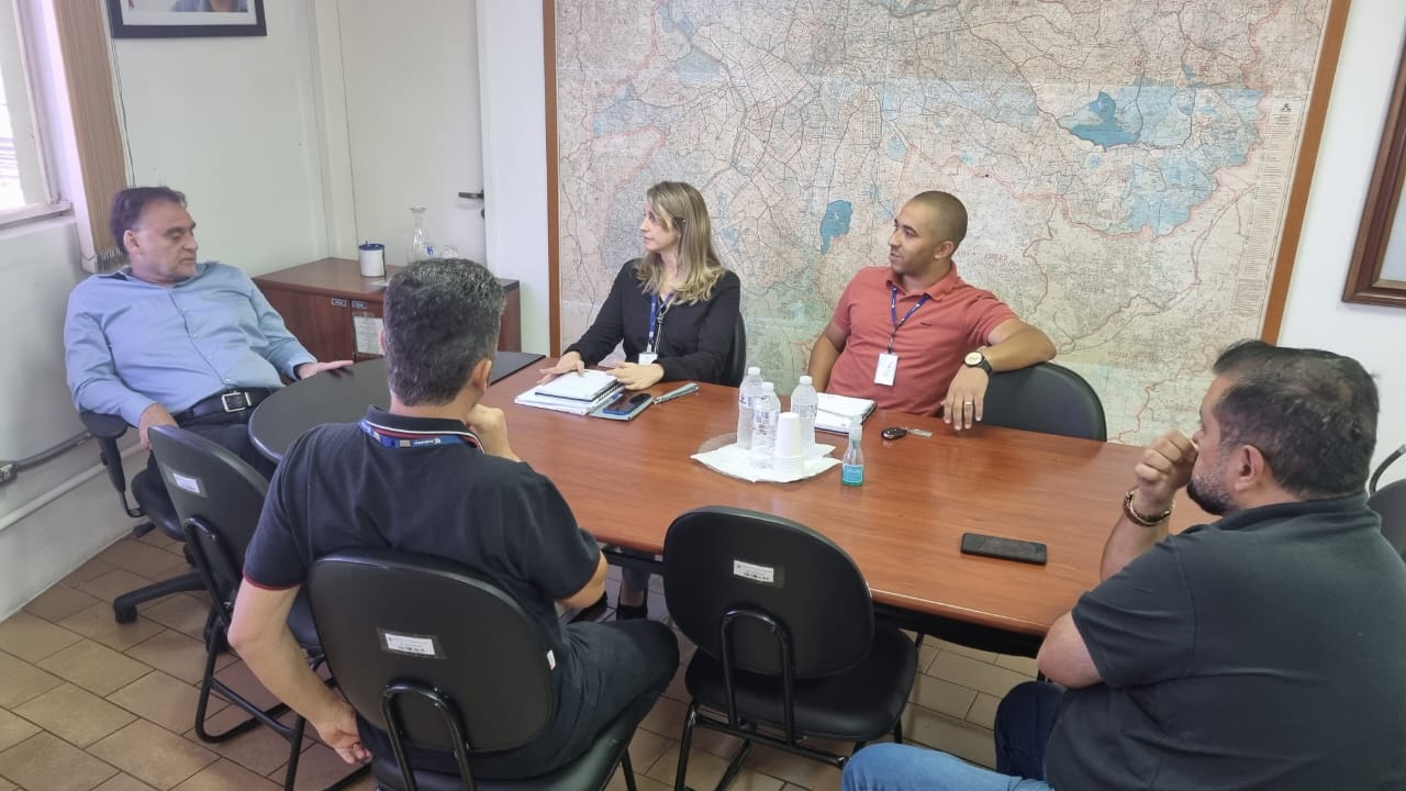 quatro homens e uma mulher estão reunidos em torno de uma mesa oval