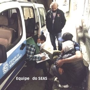 Equipe do Seas anota ados de duas pessoas numa calçada, junto ao carro da equipe