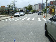 Foto da Rua Santo Américo sem desníveis, sem buracos em razão da implementação do Asfalto novo. Na foto há grande quantidade de carros nos cantos da via.