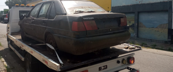 Carro preto sem placa, marca Santana, em cima de um guincho em uma rua.